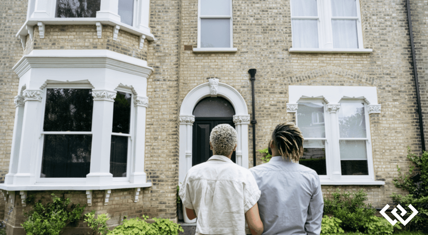 the backs of two people, looking at the facade of a brick home