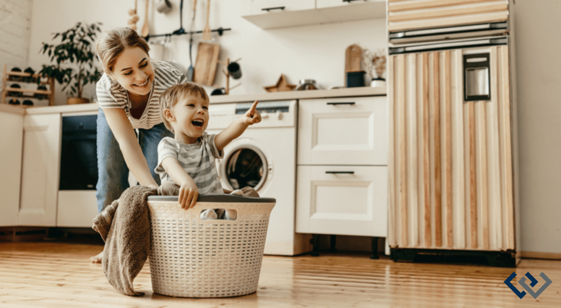 Set in a kitchen, woman appears to be pushing a child who is sitting in a laundry basket