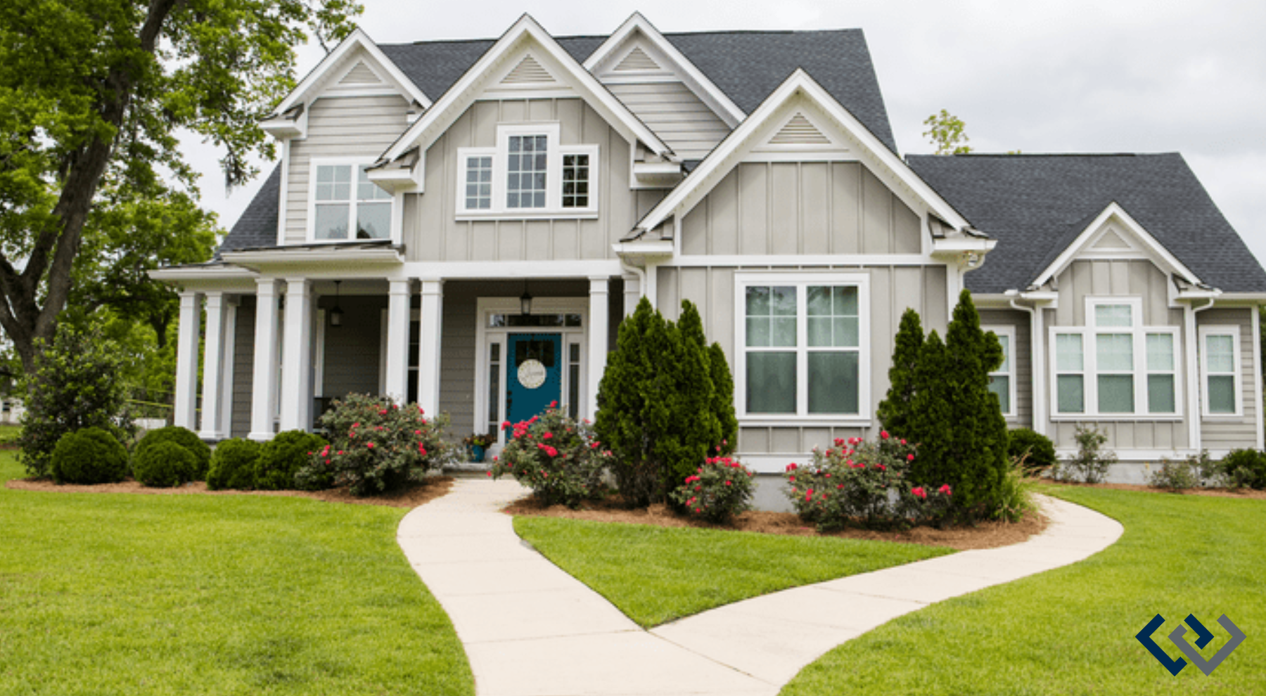 The facade of a large grey home with a manicured front lawn and plantings